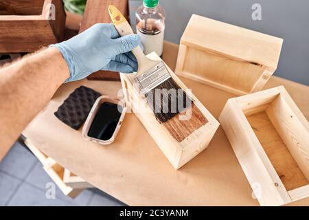 Man carpenter varnishing wooden crate for flowers with brush in her small business woodwork workshop. In your work, do you use stains or wood Stock Photo
