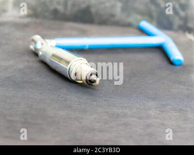 old carbon-coated spark plug in blue hinged key for spark plugs of an internal combustion engine needed at the service station Stock Photo