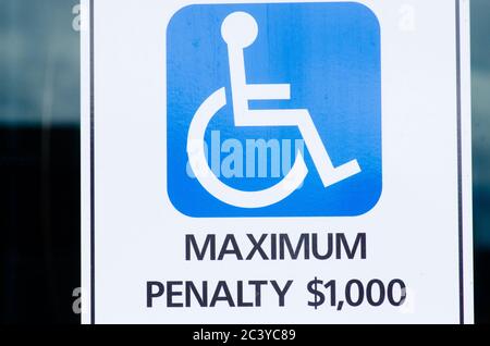 Close up of white on blue Handicapped in wheelchair sign and symbol at disabled car park with penalty warning. Stock Photo