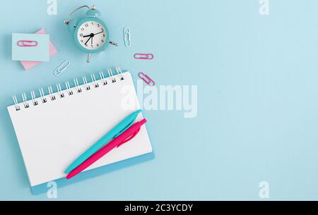 Template mockup. Workspace with notebook, clock and pens on pastel blue background. Top view. Copy space Stock Photo