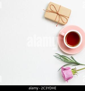 Gift box and cup of black tea with pink rose flower on white background. Flat lay, top view, copy space Stock Photo