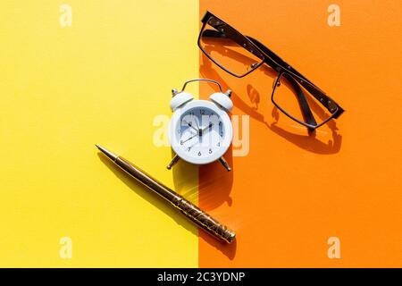 Minimalist flat lay composition of workplace desk table with supplies and alarm clock. Morning or deadline concept. Top view with space for your text Stock Photo