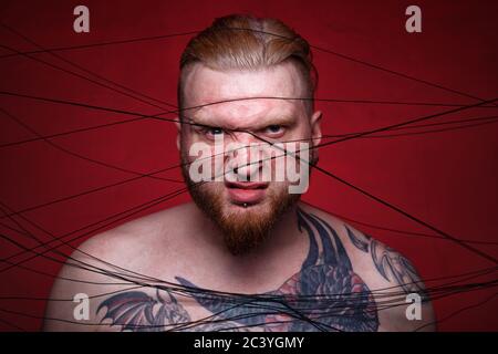 Photo of tangled in black threads bearded frowned man Stock Photo