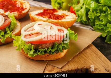 Cooking tasty grilled home made burgers with beef, tomato and lettuce opened on a wood cuttind board Stock Photo