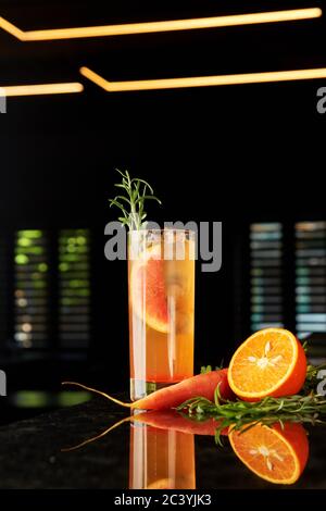 Cocktail with gin, carrot liquor, tonic, orange and rosemary and tonic on black marble bar counter Stock Photo