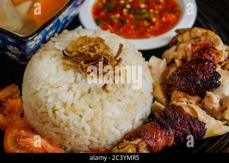 Chicken rice with chopped roasted chicken served with spicy chili sambal and chicken soup. Top up with sliced tomato and fried onion. Stock Photo