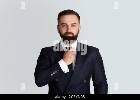 Successful businessman in office wear touching his necktie on grey background Stock Photo