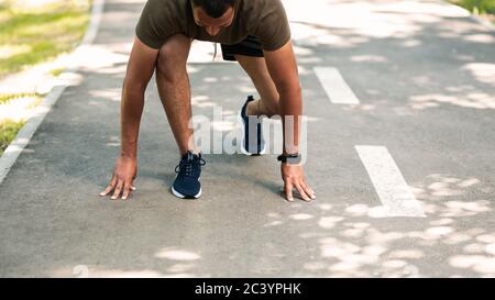 Fit African American sportsman in starting position, ready to run on jogging track outdoors, copy space Stock Photo