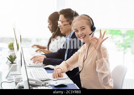 Customer service executive showing okay gesture and her colleagues working at call centre Stock Photo