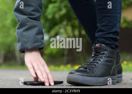 The girl finds a smartphone on the street and picks it up from the asphalt Stock Photo