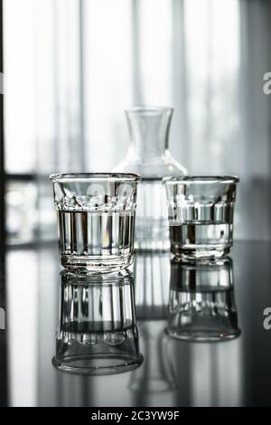 Two glasses of water and a carafe, reflectioning in a black table. Vertical image. Stock Photo
