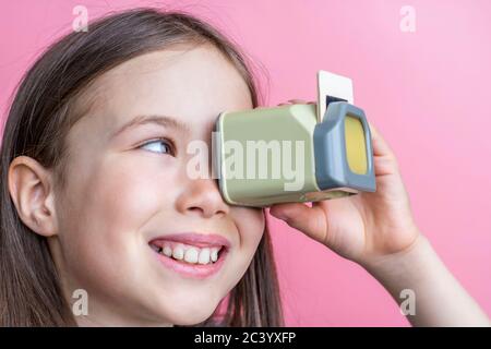 Child girl looks at old photos through a diascope. Banner template on pink background. Stock Photo
