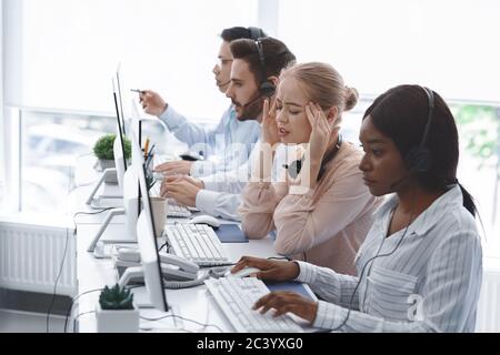 Technical support operator suffering from headache and her colleagues working with computers in office Stock Photo