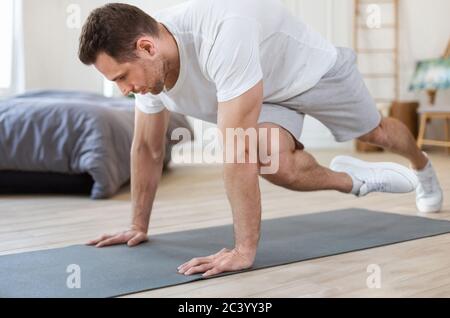 Sporty Man Training At Home Doing Running Plank Exercise Stock Photo