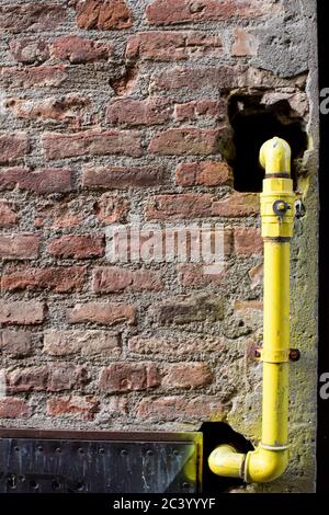 Yellow hydraulic hose coming out of a brown brick wall. Colored pipes in hydraulic system Stock Photo