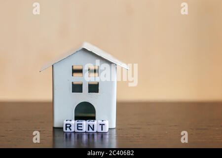 Miniature toy model house with inscription RENT letters word on wooden backdrop. Eco Village abstract environmental background. Real estate mortgage property insurance sweet home ecology rent concept Stock Photo