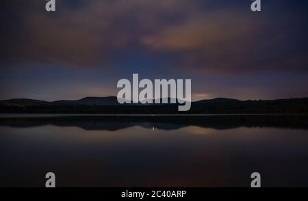 stars and clouds over lake Olbersdorfer See near Zittau, Saxony/Germany. Night landscape with Zittauer Gebirge in the background. Mountain Reflections Stock Photo