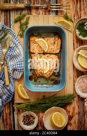 Roasted salmon in heat proof dish. With aromatic dill, lemon, salt and pepper on sides. Stock Photo