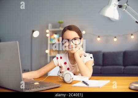 Portrait of smiling school girl studying online in living room with laptop computer. Stock Photo