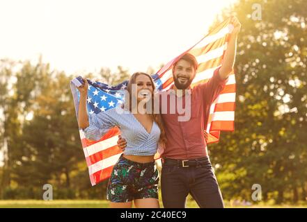 Happy couple with america flag celebrating independence day at sunset. Stock Photo