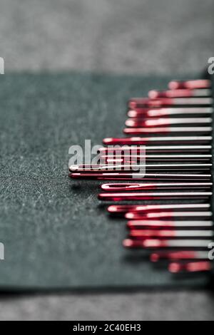 Sewing needles of different sizes in a set of red on a black background. Stock Photo