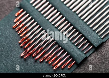 Sewing needles of different sizes in a set of red on a black background. Stock Photo