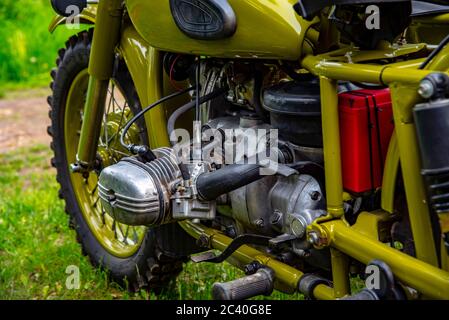 Part of a retro motorcycle, wheel and motor, on a background of green grass. Stock Photo