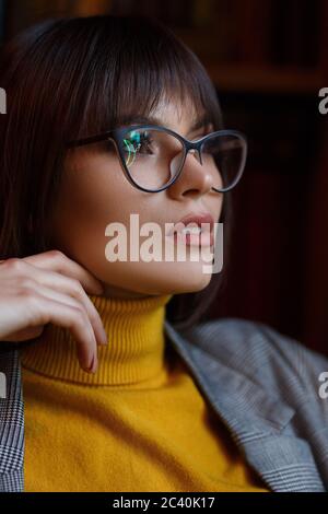 Beautiful dreamy girl in stylish sharp glasses. In the library. Stock Photo