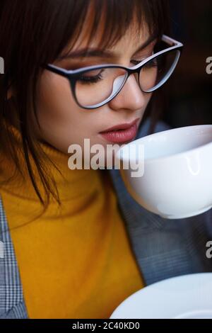 Beautiful dreamy girl in stylish sharp glasses. With a cup in his hands. Stock Photo