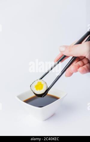 Close up of woman holding chopsticks with sushi roll and bowl with soy sauce on table, japanese traditional healthy meal concept. Stock Photo