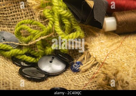 Various buttons and multicolored threads on coarse-textured burlap. Close up Stock Photo