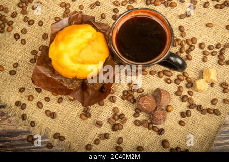 Fresh cupcake, coffee mug and coffee beans on a homespun fabric with a rough texture. Close up Stock Photo