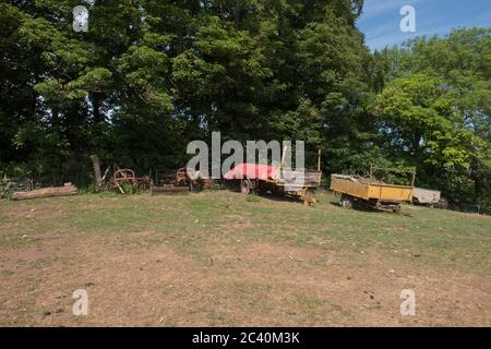 Group of Rusty Old Farm Machinery and Trailers on Top of a Hill in a Field on a Farm in Rural Devon, England, UK Stock Photo