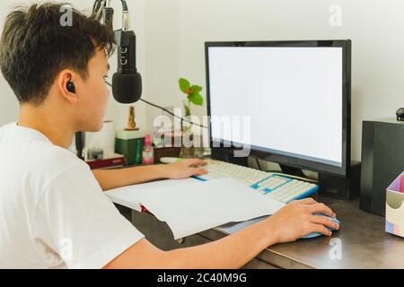 Asian teenage boy study at home uses pc online class during Quarantine and coronavirus epidemic. Stock Photo