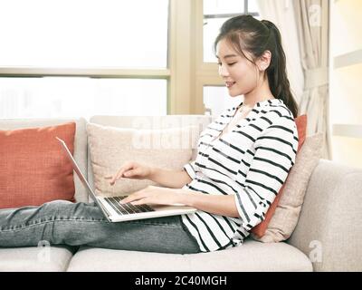 young asian woman working from home sitting on couch using laptop computer Stock Photo