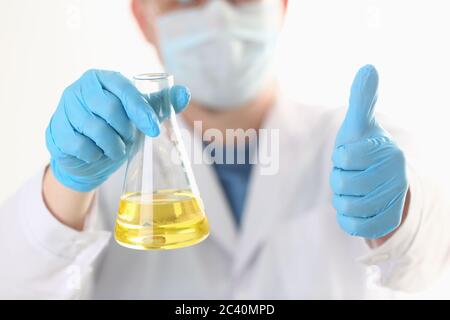 Doctor holding test tube with yellow liquid and giving thumbs up Stock Photo