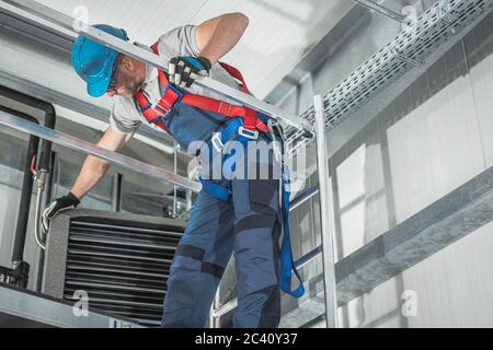 Warehouse Commercial Building Heating Device Servicing by Caucasian Technician on Scaffolding. HVAC Job. Stock Photo