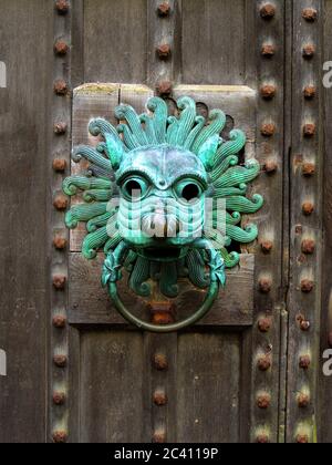 Brougham Hall (UK) decorative lion head knocker with a ring in its mouth on a studded oak  door.   It is a replica of the Durham Cathedral sanctuary knocker. By tradition, any fugitive from the law who was able to reach the door and grasp the knocker would be granted sanctuary and protected from prosecution. (recognised by English law from the fourth to the seventeenth century). Metal studs were used not only to strengthen the door but also to add to its decorative appearance. Though  the incredibly ornate bronze knocker we see today is exactly the same in every respect as the stolen  original Stock Photo