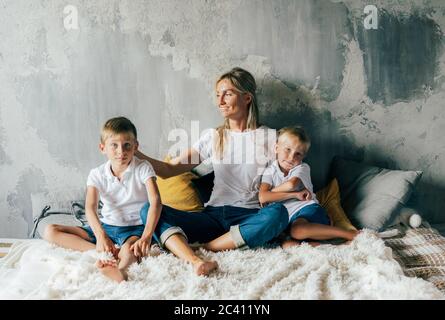 A caring mom sits on the bed and gently hugs her sons. Parenting and caring for children. Family content. Conscious parenthood and childhood.  Stock Photo