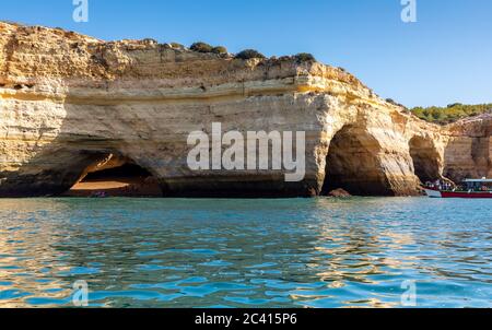 Landscape with the famous Benagil Caves, clear blue sky, sandstone cliffs and tour boat on the Algarve coast in Portugal Stock Photo