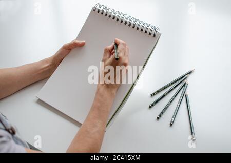 Woman drawing in a sketchpad. Close up view. Pencils on the table. Right handed Stock Photo
