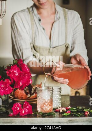 Young woman pouring rose lemonade to glasses over kitchen counter Stock Photo