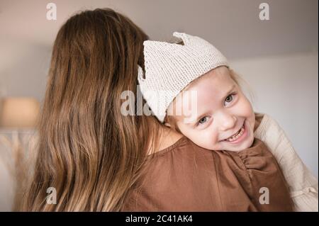 Girl putting head on mother shoulder smiles and looks away camera.