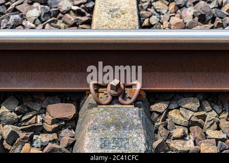 Railroad tracks lying on concrete sleepers, filling between large pieces of rock, close-up on the fastening screw. Stock Photo