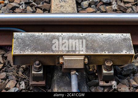 Automatic train braking system mounted on railway tracks, visible concrete sleepers and large stones between them. Stock Photo