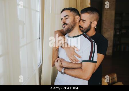 homosexual couple hugging at home by the window Stock Photo