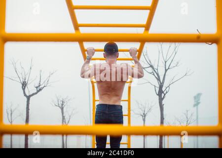 man with cap doing pull-ups in a calisthenics park. back photo Stock Photo