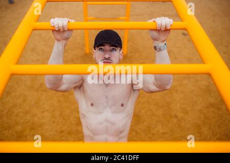 man with cap doing pull-ups in a calisthenics park. high angle Stock Photo