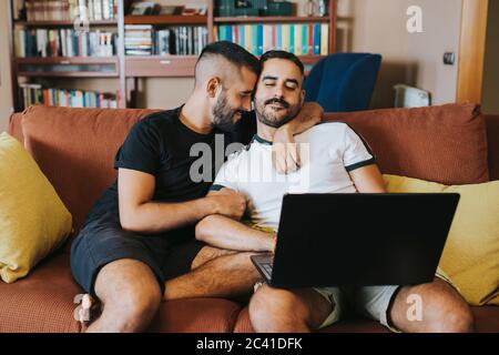 romantic gay couple using laptop on sofa Stock Photo