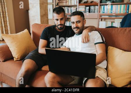 gay couple sitting on the couch looking at the laptop Stock Photo